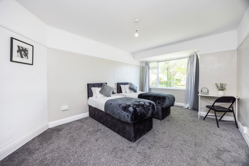 Bright bedroom with two single beds, grey carpet, chair and window with garden view