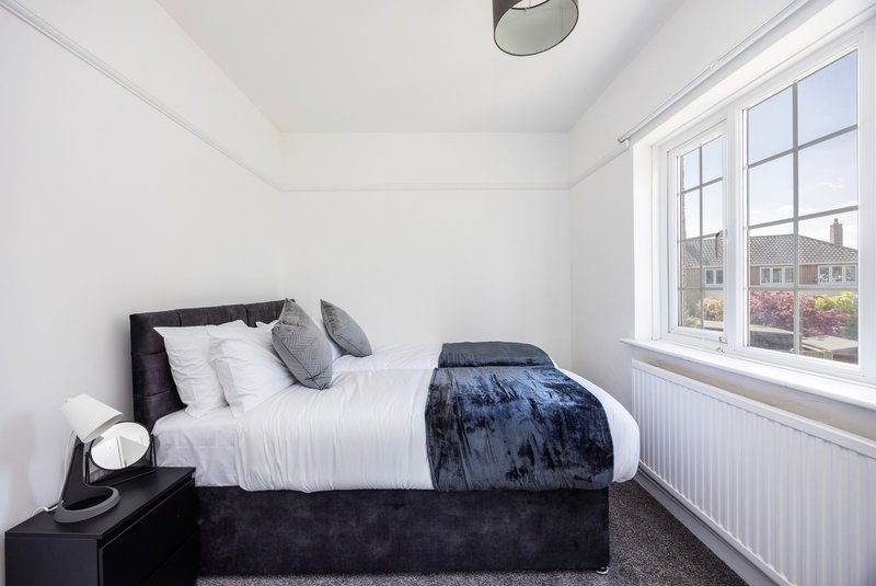 Bright bedroom with double bed, black headboard, white bedding, and large window overlooking street