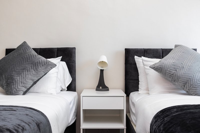 Twin bedroom with matching black headboards, white bedding, grey pillows and central nightstand