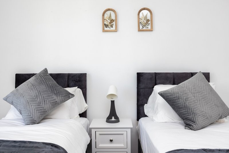 Twin bedroom with grey headboards, white bedding, patterned cushions and wall art