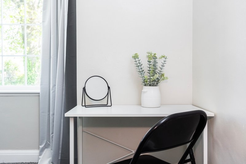 Minimalist desk with mirror, potted plant, and black chair by window
