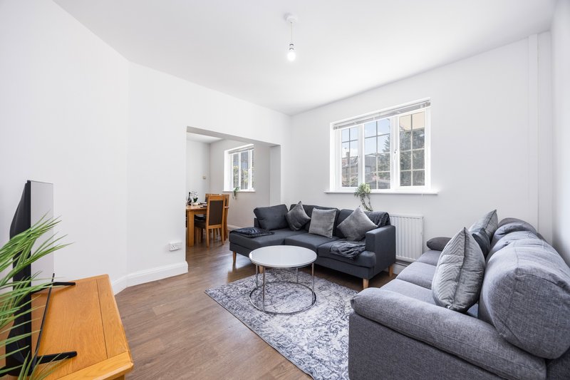Bright living room with dark sofas, white walls, wooden floor and large windows