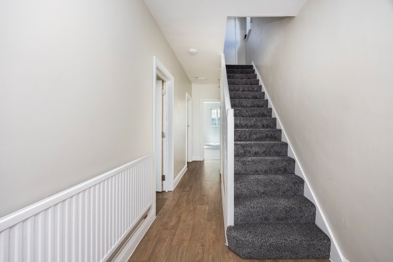 Hallway with wooden floor, white walls, radiator, and staircase with grey carpet