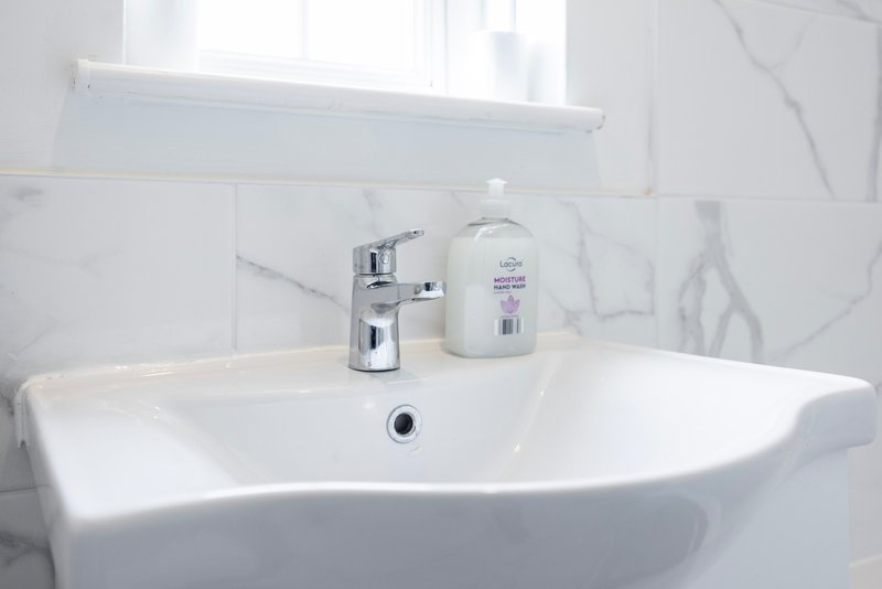 Modern bathroom sink with chrome tap, soap dispenser and mirror above marble tiles