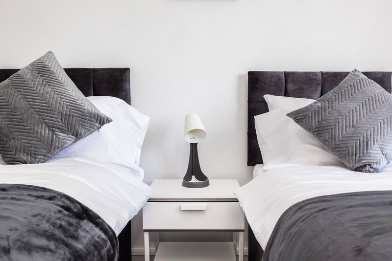 Twin bedroom with grey upholstered headboards, white bedding, patterned cushions and shared nightstand