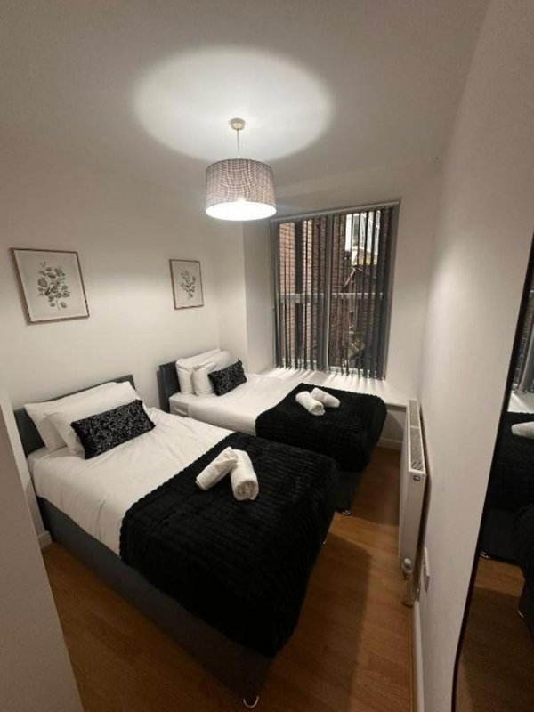 Modern bedroom with two single beds, black throw blanket, pendant light fixture and framed wall art