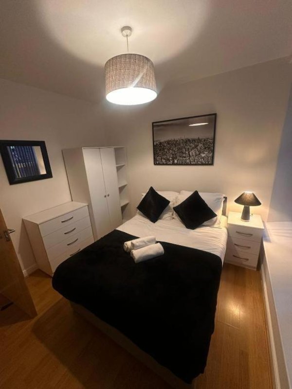 Modern bedroom with double bed, black throw, white furniture, pendant lamp and framed wall art