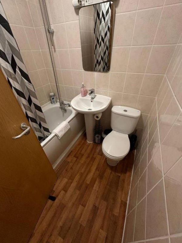 Bathroom with toilet, sink, bathtub, geometric shower curtain and wooden flooring