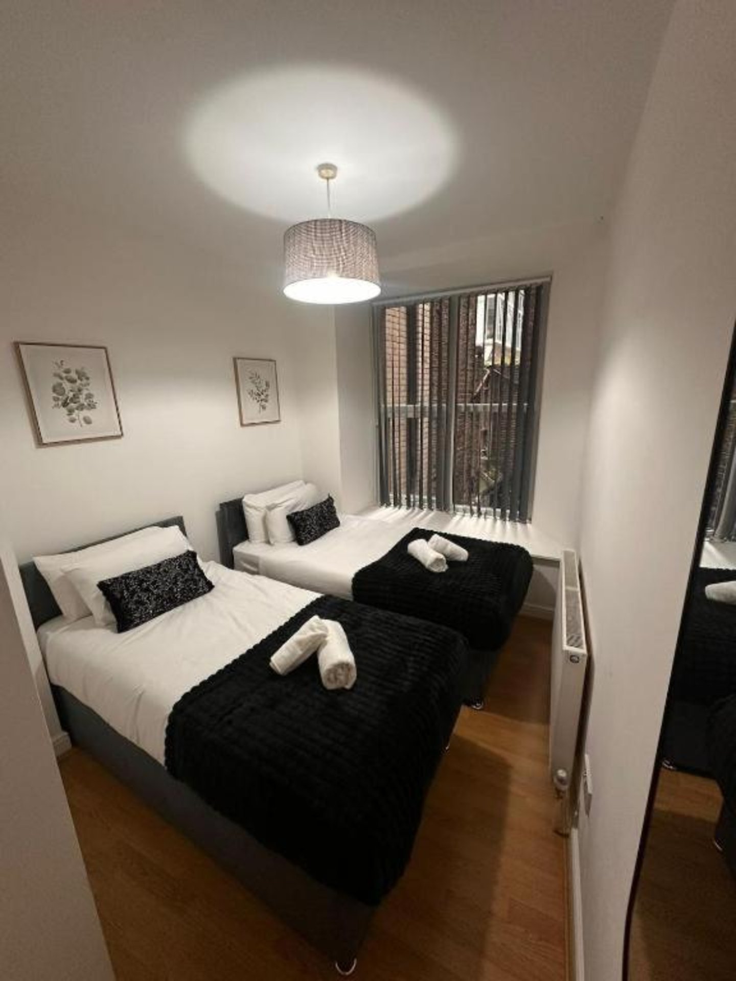 Modern bedroom with two single beds, black throws, pendant light and framed wall art