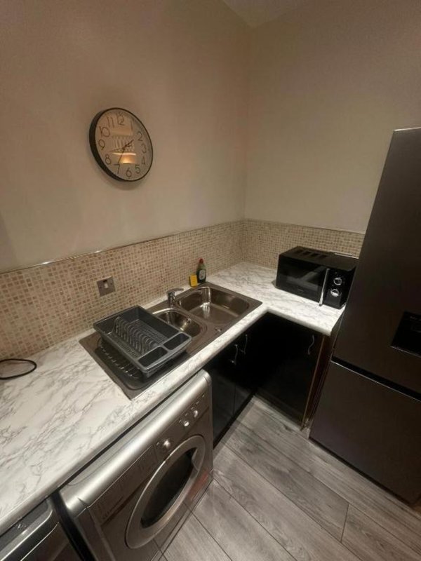 Kitchen with sink, washing machine, black microwave, refrigerator and wall clock