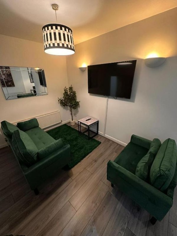 Modern living room with two green sofas, wall-mounted TV, pendant lamp and wooden flooring