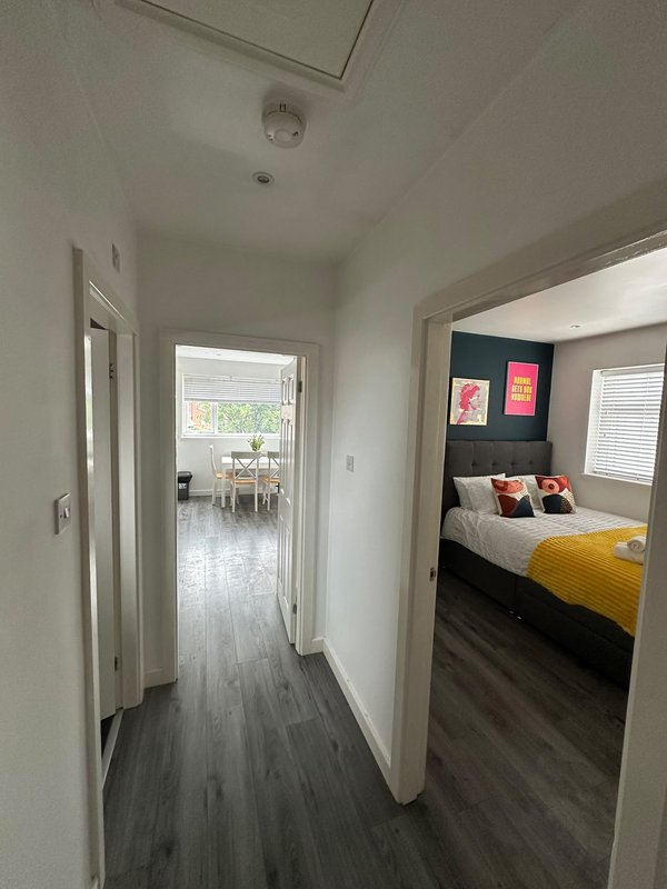 Hallway with white walls, dark wood flooring, leading to bedroom and living areas