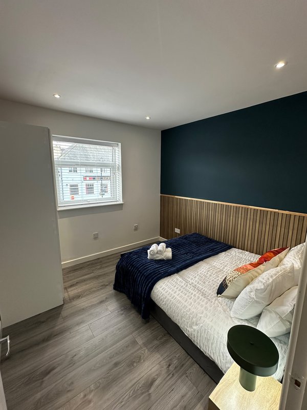 Modern bedroom with two beds, dark accent wall, wooden headboard paneling and window