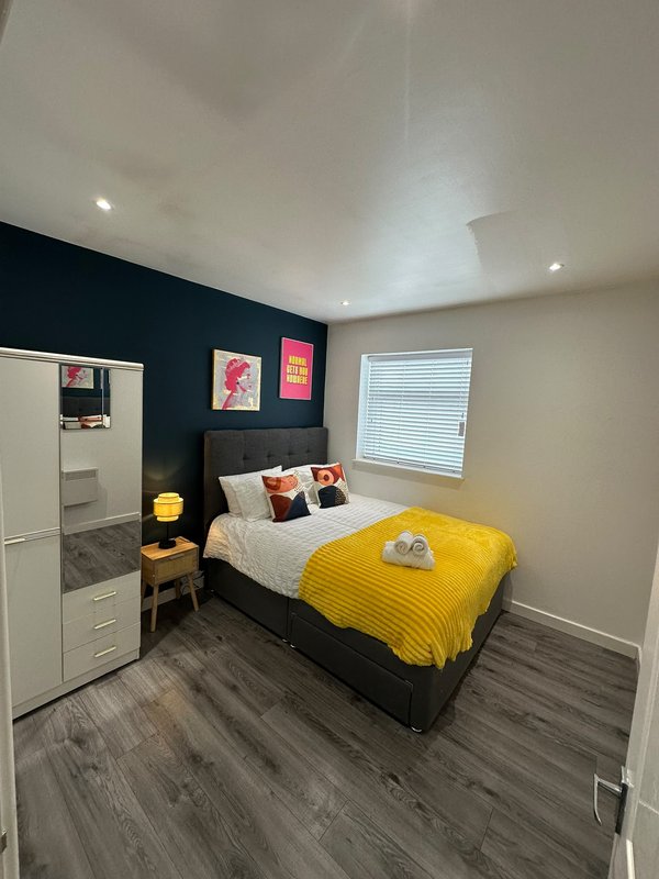 Bedroom with double bed, yellow bedding, dark accent wall, white wardrobe and bedside furniture
