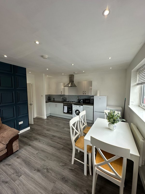 Open-plan kitchen and dining area with white table, chairs, black cabinetry and stainless steel appliances