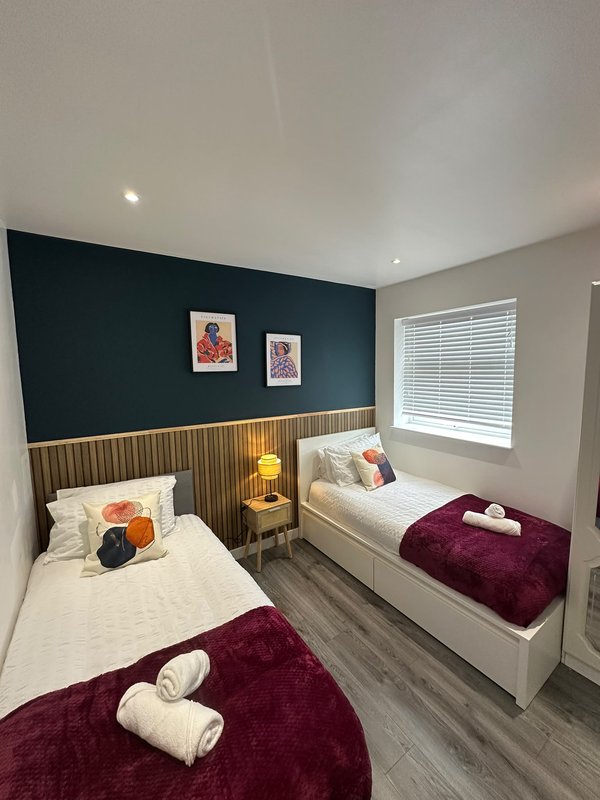 Modern bedroom with two single beds, dark teal accent wall, wooden headboard paneling, and contemporary furnishings