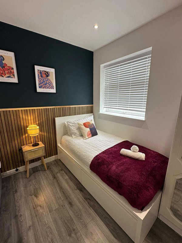 Modern bedroom with single bed, dark blue accent wall, wooden panelling, framed artwork and bedside lamp